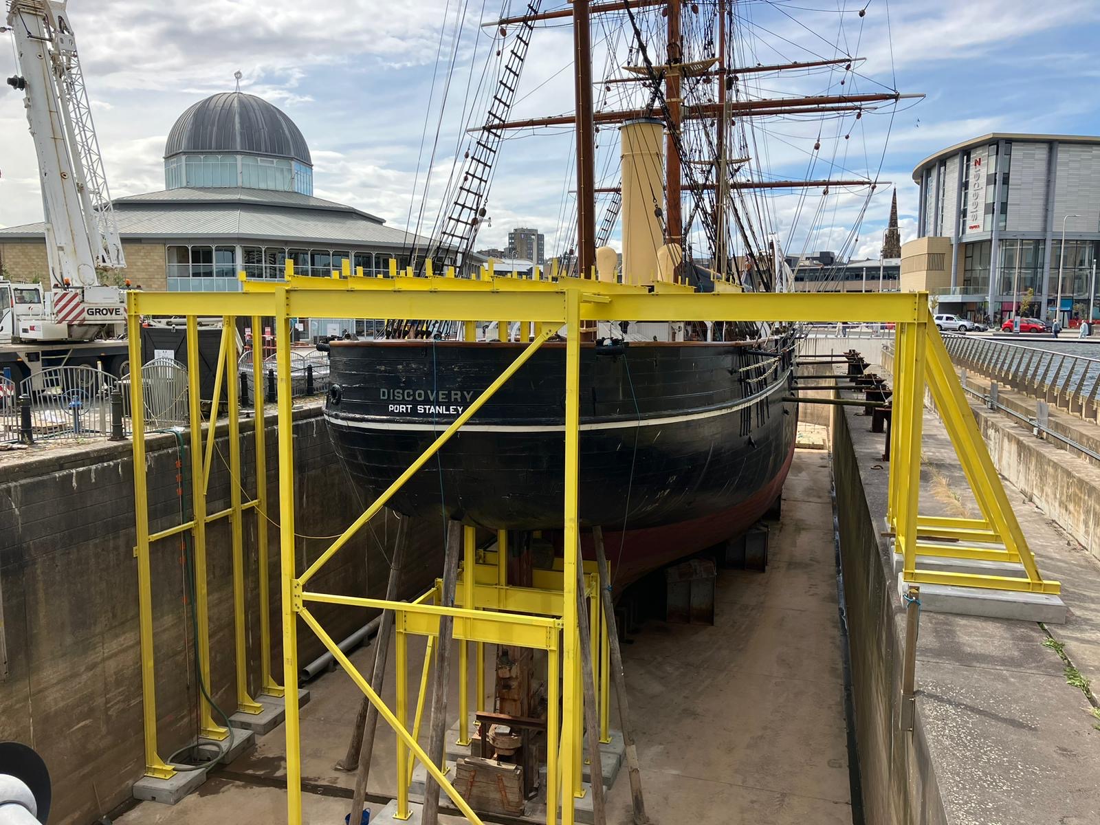 A temporary yellow scaffold protrudes around the stern of the Royal Research Ship Discovery in its dry-dock.